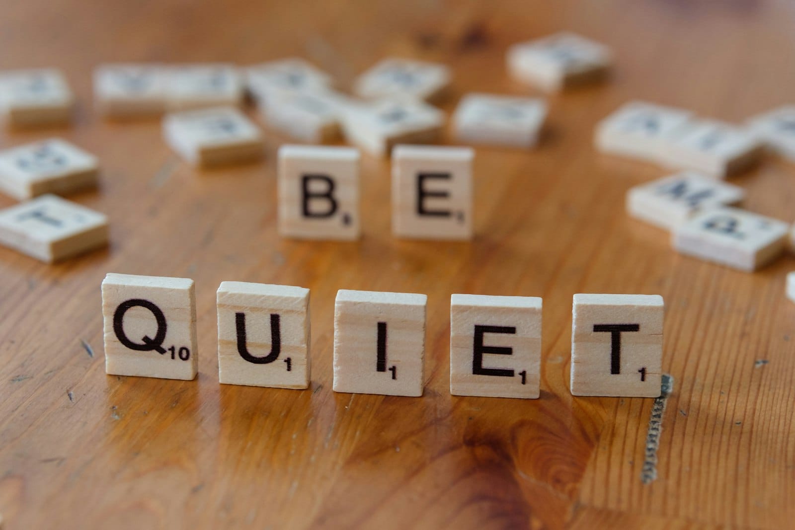 The word be quiet spelled with scrabble letters on a wooden table