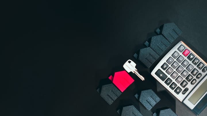 A silver key, a red house model, and a calculator on a black surface